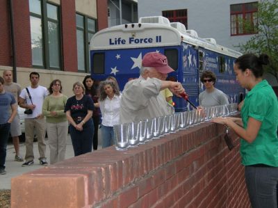 Jaan Holt, program director, Architecture, lights candles for each of the victims as their names are placed under glass holders. 